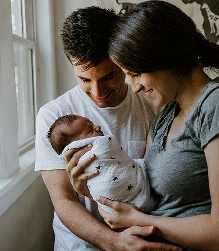 		 A father and a mother smiling at a baby she is holding
	