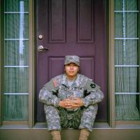 Person wearing fatigues sitting on a porch