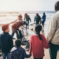Man with children watching others pulling nets in from the sea