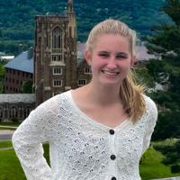 Catherine Cherry in a white sweater, smiling, with Cornell's Libe Slope in the background.