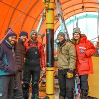 Four people in winter gear stand around a tall, thin piece of equipment