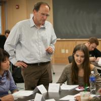 Steven Strogatz standing next to a table of students who are working on a math problem