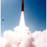 A missile on a column of smoke as it is launched into the blue sky.