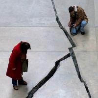  A kneeling man and a standing woman gaze at a broad crack in the pavement