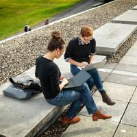  A man and woman sitting on the terrace of Olin Library, working on their computers