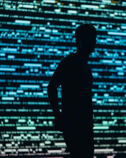 person silhouetted against a backgrond of green and blue lights