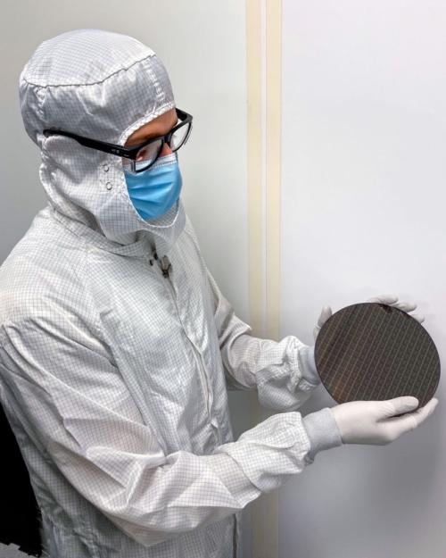 Person in white laboratory clean suit holds up a black disk