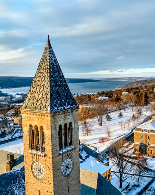 Clock tower in foreground, snowy college campus in the distance, seen from above in low light