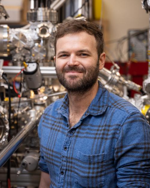 Person in blue shirt stands in front of complicated silver equipment