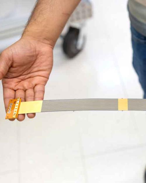 Two hands holding out a wide strip of plastic with lines running down it and connectors on either end.