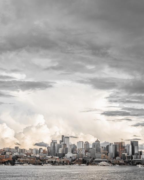 		Grey city buildings look very small compared to billowing steel- and linen-colored clouds filling the sky above
	