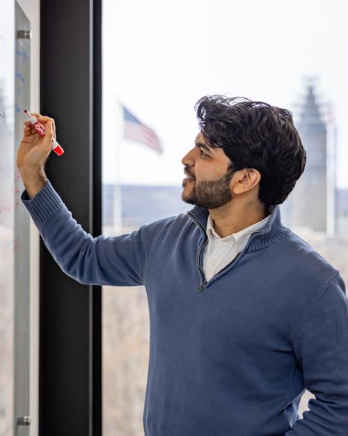 		Person writing on a dry-erase board with a window in the background
	