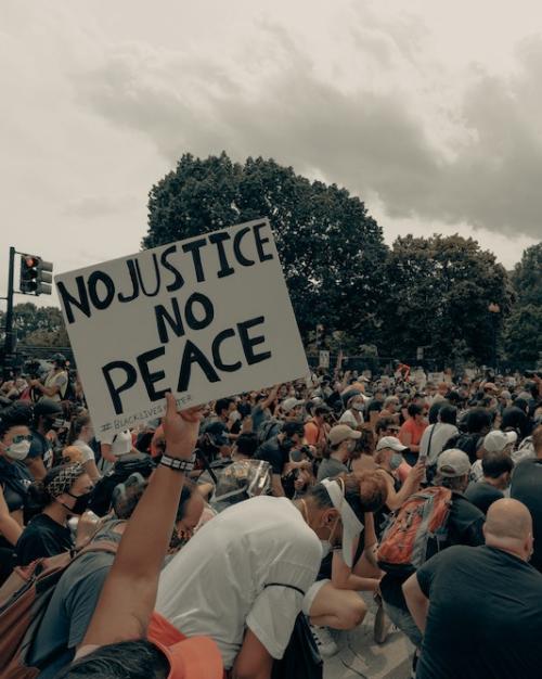 Hand-lettered sign "No Justice, No PEACE" held by a person in a crowd