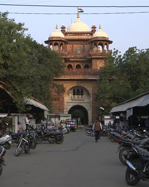 A gold building foregrounded by rows of stalls and many parked motorcycles