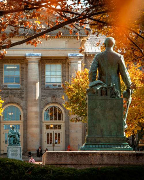 Statue facing a campus building; fall foliage