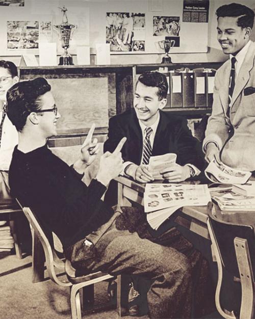 Black and white historic photo of a half dozen young men, relaxing togther around a table