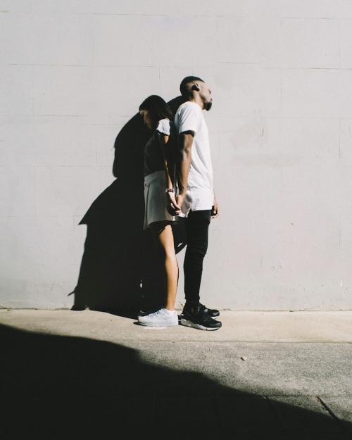 Two people leaning back to back against a wall, shadowed