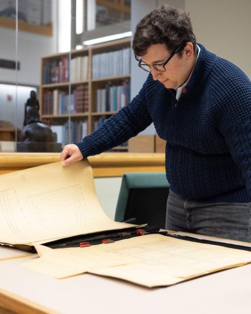 		Person holds a large, yellowed document in a library setting
	