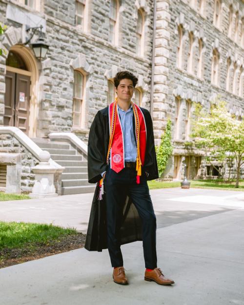 		Smiling photo of smiling man with Cornell graduation gown in front of academic builing.
	