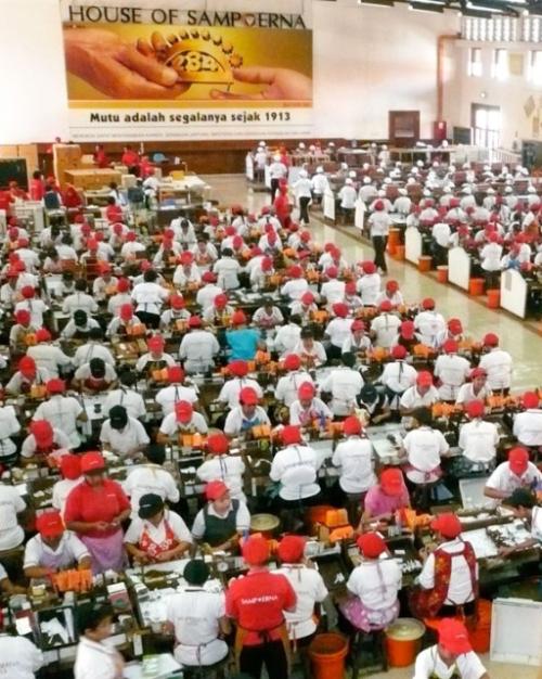 		hundreds of workers wearing red caps bend over long tables, rolling cigarettes
	