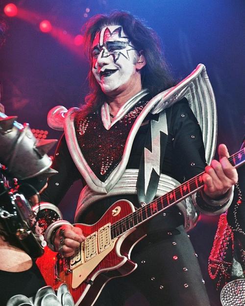		Person wearing white and black makeup and a silver and black costume, playing an electric guitar
	
