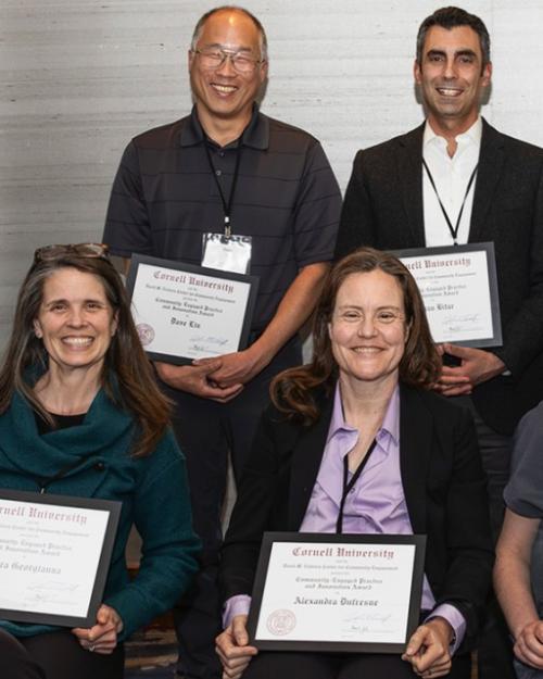 Eight people in two rows, each displaying an award certificate
