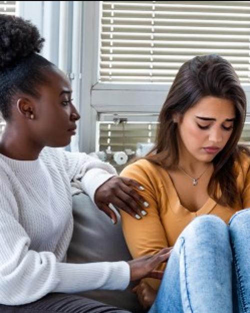 		Two people sitting on a couch, one comforting the other
	