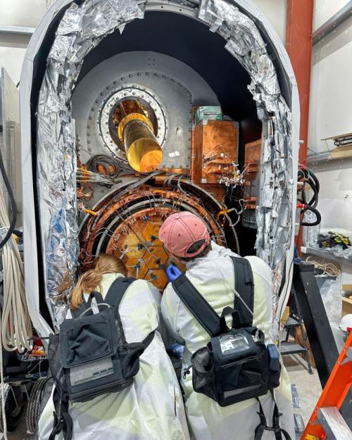 the backs of two people who are facing a large opening containing a scientific instrument, to work on it. 