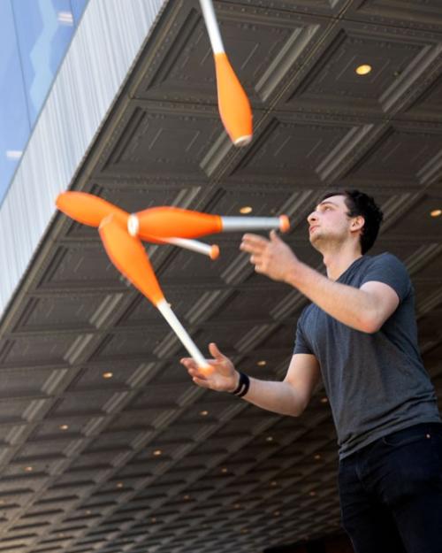 		Person juggling four orange clubs under a dark overhang
	