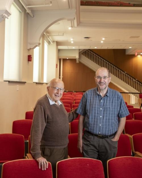 		Roald Hoffmann standing in a big lecture hall with one hand on Jeff Fearn's back, with the periodic table on the wall to their left, both smiling and rdressed casually.
	