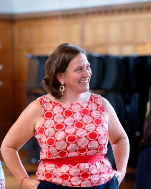 Person in red shirt smiles, hands on hips, while speaking with a circle of other people