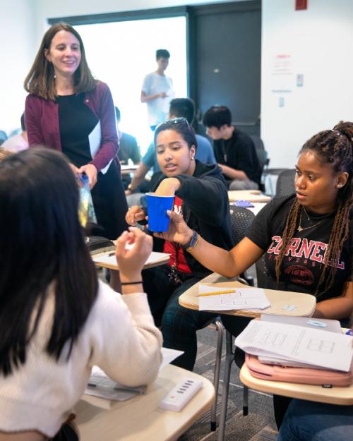 		About six students sit in desks and interact using a blue Solo cup while an instructor stands by
	