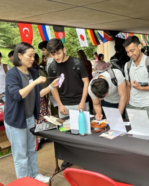 		Several people cluster around a table with international flags in the background
	
