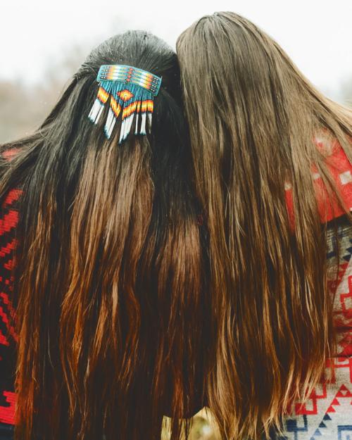 		Two women with long hair and wearing Native American-patterned clothing and hairpiece.
	