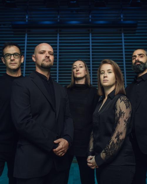 		Five people wearing black pose against a blue and black background. They look forboding.
	