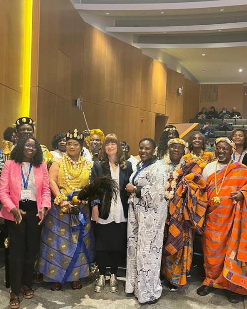 		Sevral people, some in colorful traditional dress, stand together in an auditorium
	