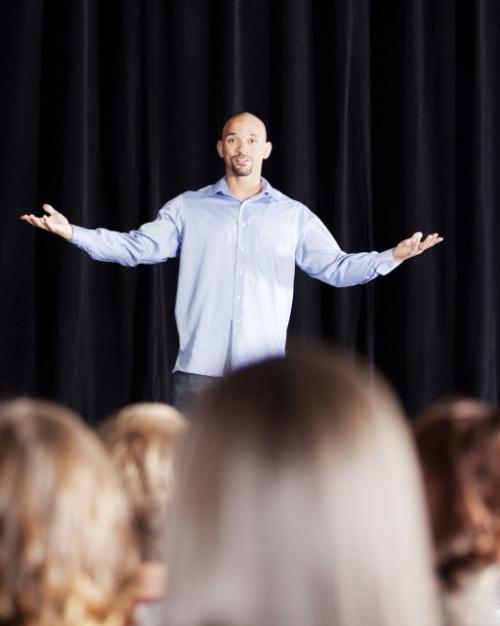 Person standing on a stage with arms spread