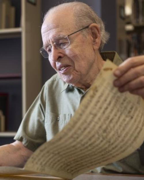 		Neal Zaslaw, in glasses and short-sleeved button-down shirt, looking at a musical score long enough that he is holding it in both hands.
	