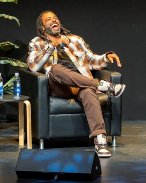 		Two people on a stage, sitting in arm chairs, holding microphones
	