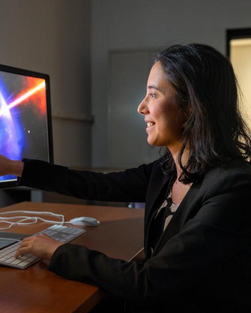 Anna Ho sitting at desk, pointing at computer screen with image of star exploding