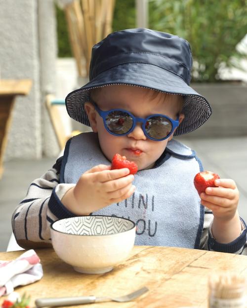 		child wearing sunglasses, holding two strawberriers
	