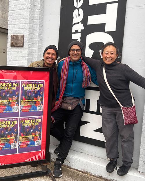 		Three people stand near a red production poster outside a theater
	