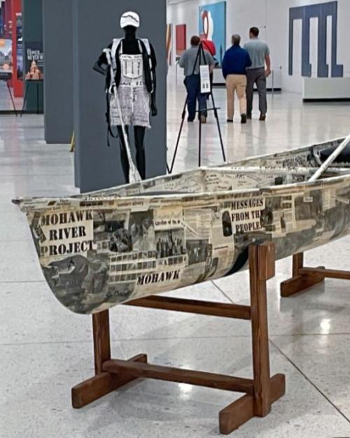 A canoe covered in written messages, in an exhibit hall