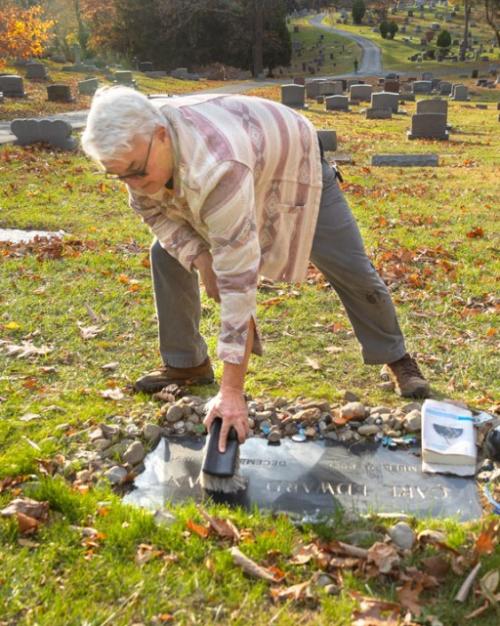 Person bending over to sweep a flat grave marker