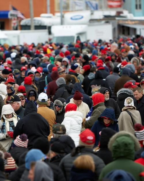 		hundreds of people crowded together, waiting for a public event to being. It is cold; most of them wear hats and coats
	