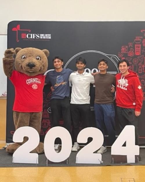 		Four people stand with a mascot bear 
	