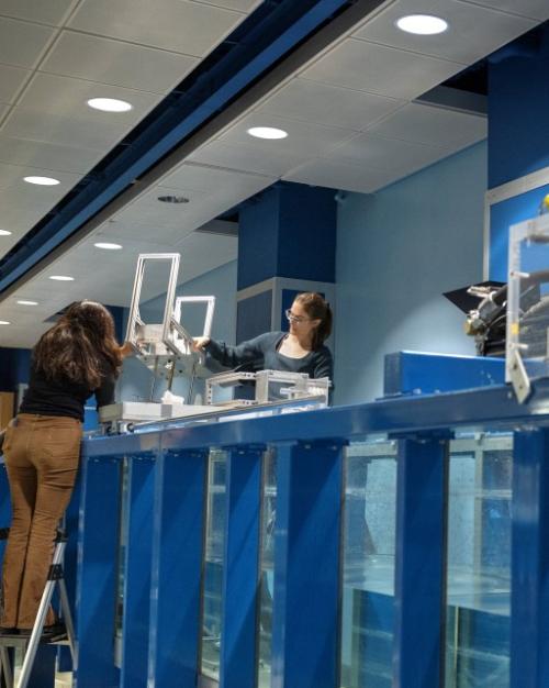 		Two people work on a very large piece of equipment that's blue and holds a lot of water
	