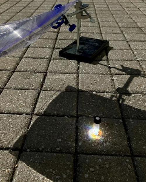 		A glass vial sits in a patch of sunlight on a square tiled floor, with shadow around it.
	