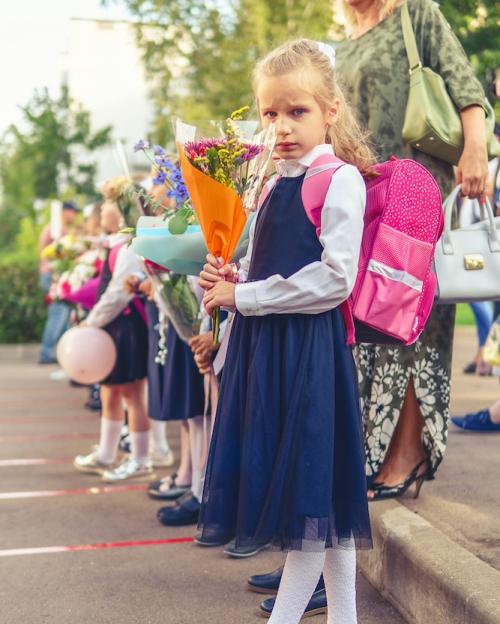 		Girl wearing a backpack and holding flowers, in a line of other students
	