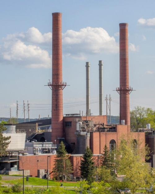 		large brick building with smoke stacks reaching into a blue sky studded with clouds
	